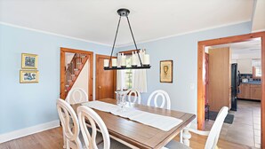 A dining area with a wooden table, white chairs, and a hanging light fixture.