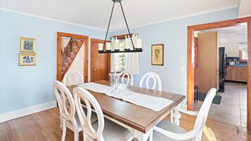 Un espace repas avec une table en bois, des chaises blanches et un luminaire suspendu.