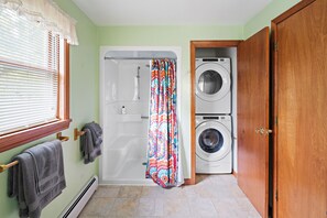 Een badkamer met een douche, een wasmachine en een deur.