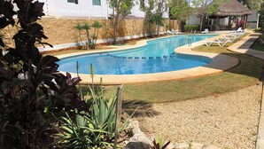 Una piscina con borde curvo, rodeada por un camino de guijarros y un césped.