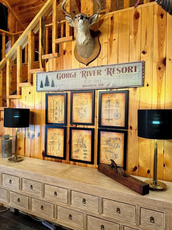 A wooden wall with a mounted deer head, framed patent drawings, and a sign reading "Gorge River Resort." - Rustic 5 Bedroom Gorge River Resort (Walhalla)
