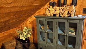 Une pièce en bois avec un plafond en pente, un meuble avec des portes en verre et une plante posée sur le sol.