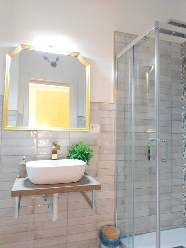 Un baño con un espejo grande, un lavamanos blanco y una cabina de ducha con paredes de vidrio.