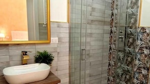 Un baño moderno con cabina de ducha de vidrio, un lavabo blanco y un espejo grande con marco dorado.