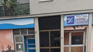 Un edificio con escaparate que dice 'PISCINA AMICI NUOTO' y un paso de peatones.