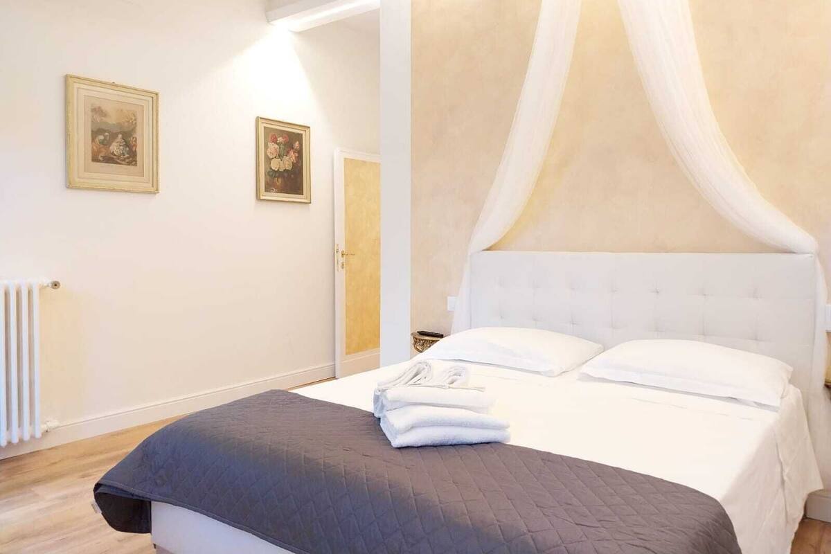 A bedroom with a bed, white curtains, and two framed pictures on the wall.