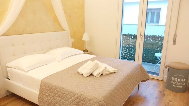 Un dormitorio con cama, mesita de noche, lámpara y vistas al exterior a través de una puerta corredera.