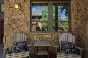Eine Steinsäule mit einem Fenster, zwei Adirondack-Stühle mit gemusterten Kissen und ein kleiner Tisch.