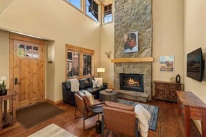 Un salon chaleureux avec une cheminée en pierre, des meubles en bois et une grande fenêtre donnant sur la cour intérieure.