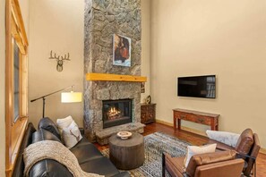 Ein gemütliches Wohnzimmer mit Kamin aus Stein, Ledersofas, einem Couchtisch und einem flachbildfernseher an der Wand.