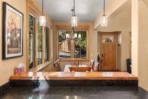 A kitchen with a granite countertop, wooden dining table, and pendant lights.