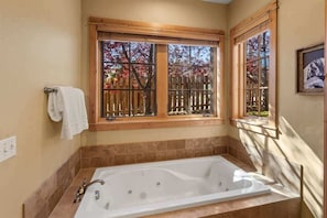 A bathroom with a large bathtub, wooden window frames, and a view of trees.
