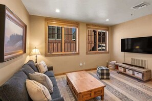Una sala de estar con sofá, mesa de centro, televisor y ventana con contraventanas de madera.
