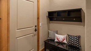 A hallway with a wooden door, a dark console table with decorative pillows, and a wall-mounted shelf. - 3-Bed Townhome in Big Sky Town Center (Big Sky)