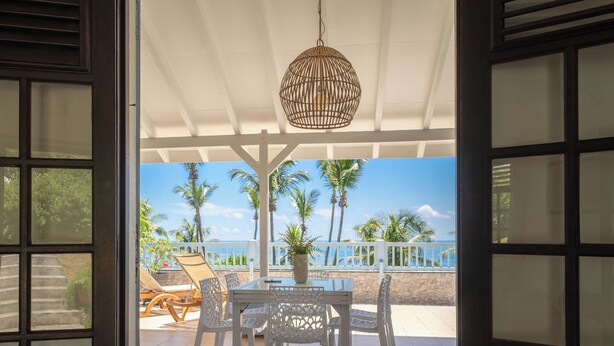 Een open terras met een tafel en stoelen, een hanglamp en uitzicht op de oceaan met palmbomen.