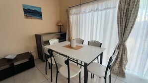 A dining area with a white table and black chairs, a small cabinet, a lamp, and a painting on the wall. - Value for Money Apartment in Newcastle (Newcastle)