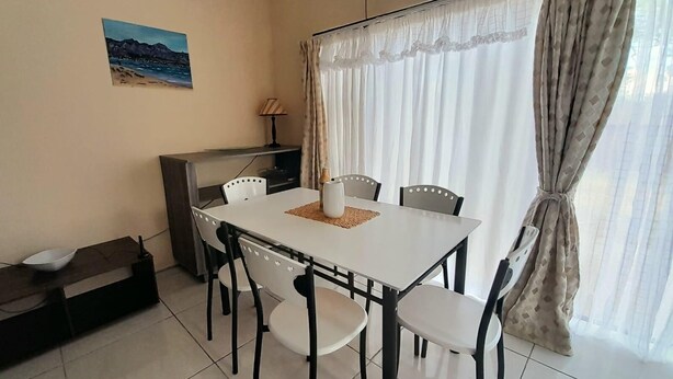 A dining area with a white table and black chairs, a small cabinet, a lamp, and a painting on the wall. - Value for Money Apartment in Newcastle (Newcastle)