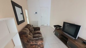 A living room with a brown sofa, a TV on a wooden stand, and a white door in the background. - Value for Money Apartment in Newcastle (Newcastle)
