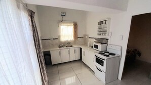 A compact kitchen with white cabinets, a stove, a microwave, and a window with curtains. - Value for Money Apartment in Newcastle (Newcastle)