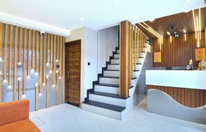 A modern reception area with a wooden reception desk, a staircase with black steps, and a wooden wall with vertical slats. - Nav Durga Guest House (New Delhi)