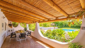An outdoor dining area with a wooden pergola, brick flooring, and a view of a swimming pool.
