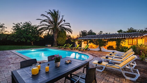 A poolside area with a table, chairs, lounge chairs, and a building in the background.