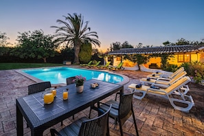 A poolside area with a table, chairs, lounge chairs, and a building in the background. - Comfort villa with pool in Albufeira (Albufeira)