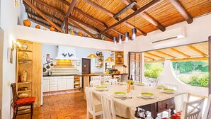 Un coin repas avec une table dressée pour quatre personnes, des chaises blanches et une cuisine en arrière-plan.