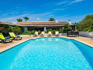Une piscine avec des chaises longues, un espace patio et un bâtiment doté d’un toit en tuiles.