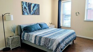 Un dormitorio con cama, mesita de noche, lámpara y una obra de arte.