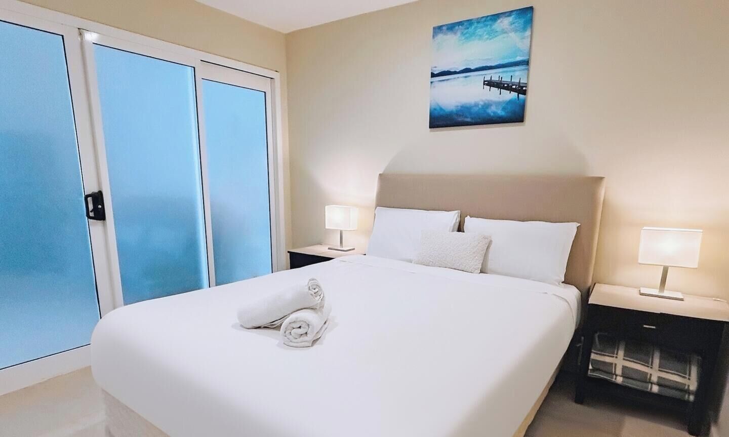 Ein Hotelzimmer mit einem Bett, zwei Nachttischlampen, einem Bild und Blick durch eine Schiebetür.