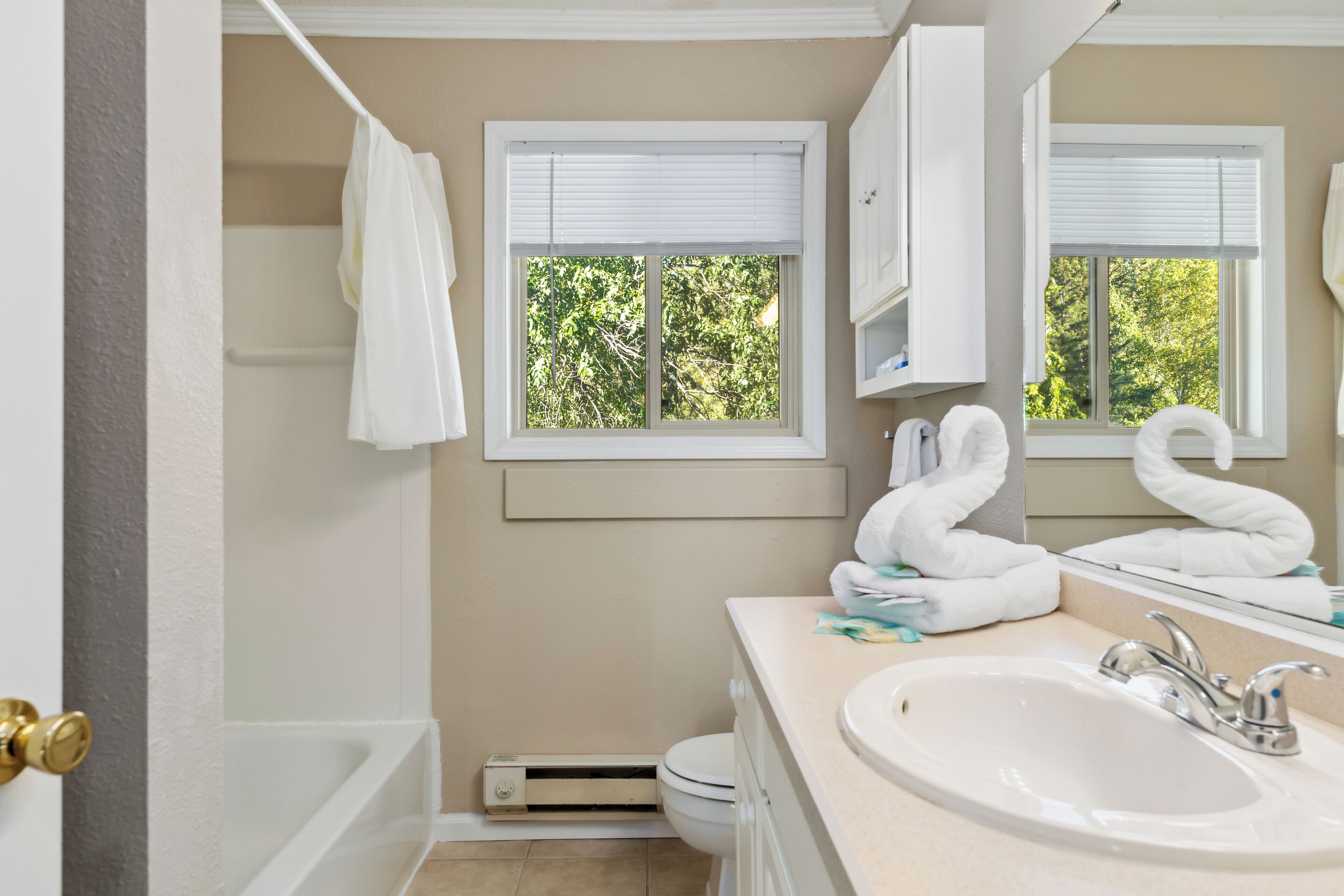 Un baño con bañera, lavamanos y dos ventanas con persianas.