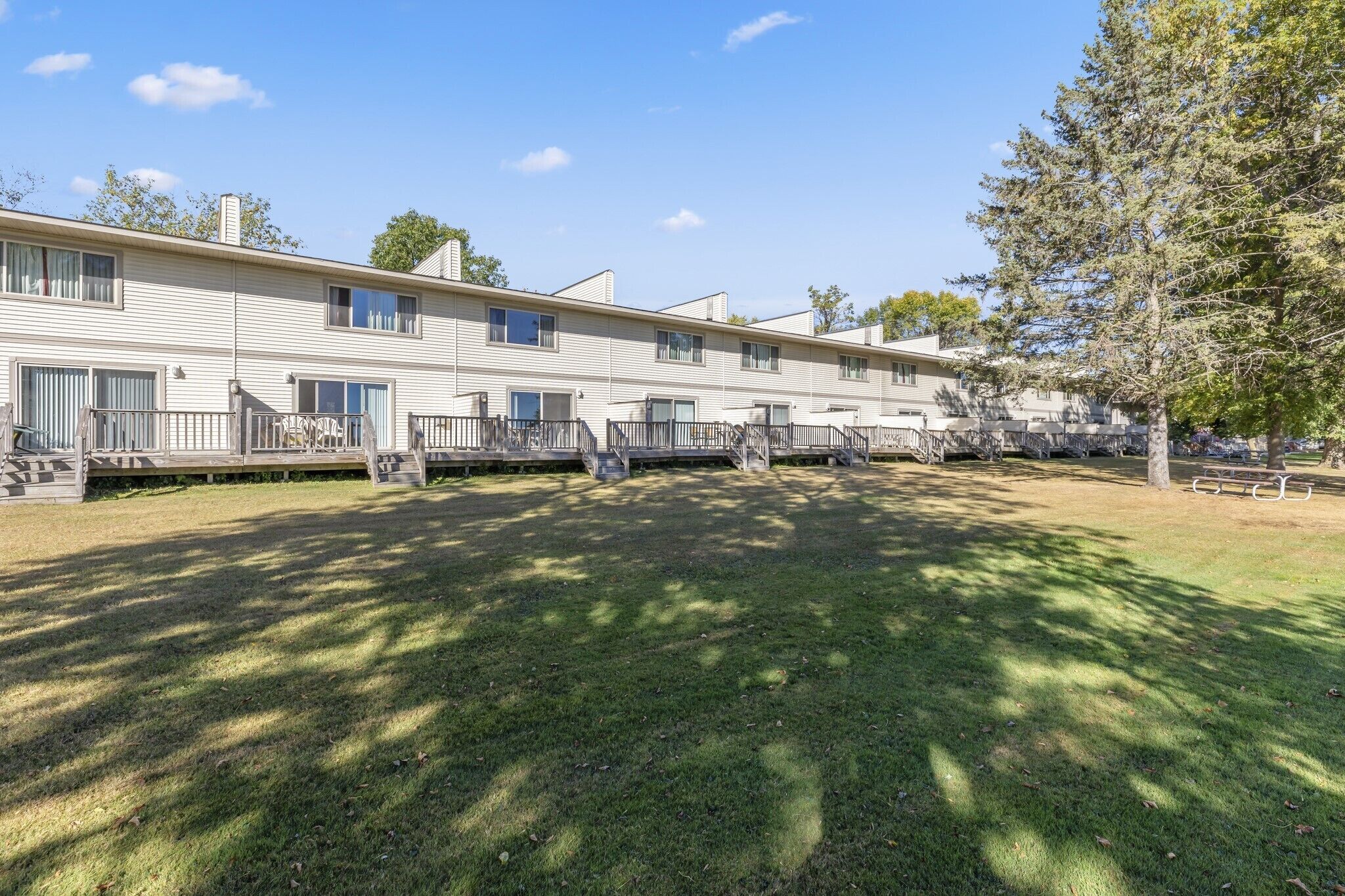 A row of single-story mobile homes with a grassy yard and trees.