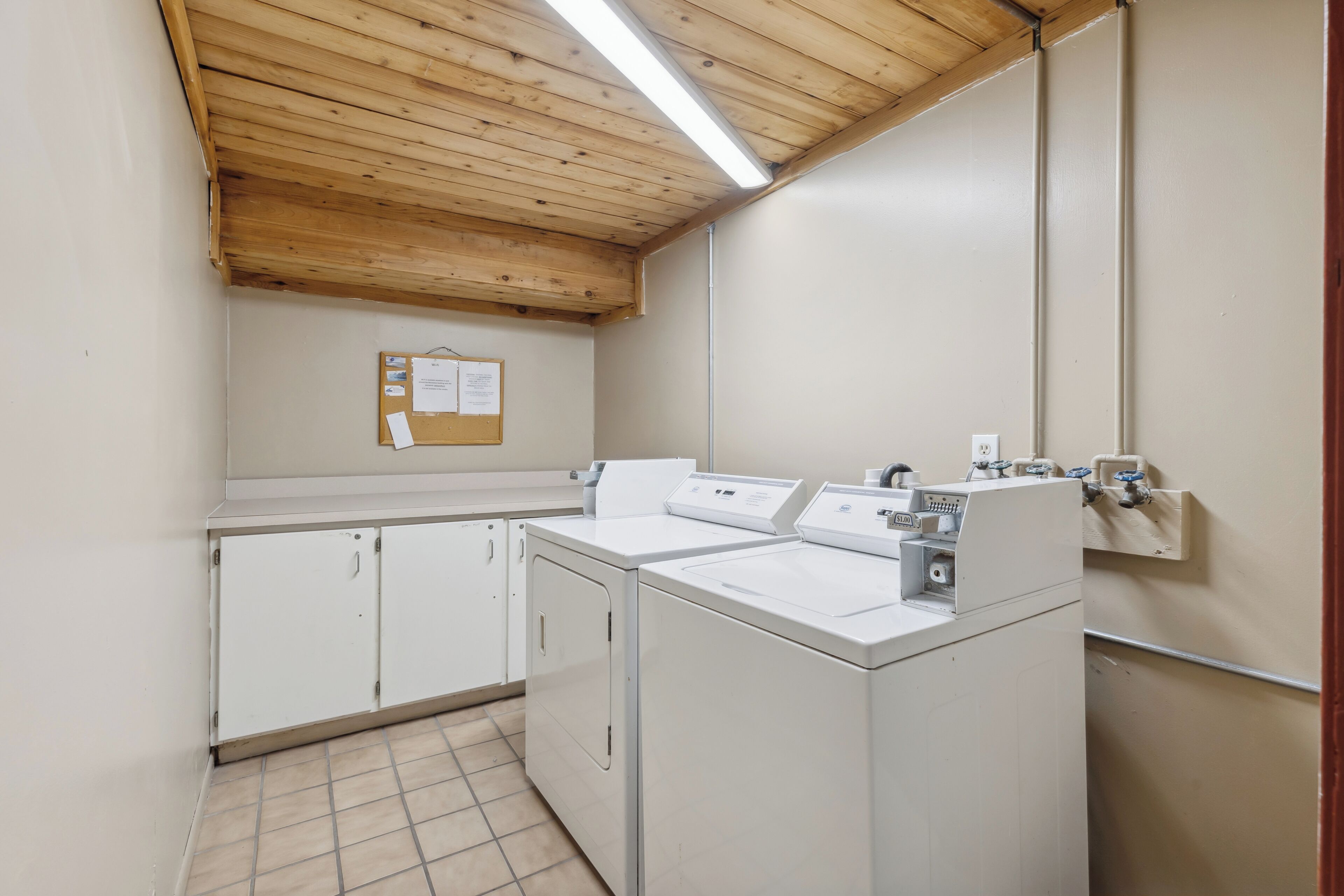 Una lavanderia con due lavatrici, una bacheca e un soffitto in legno.