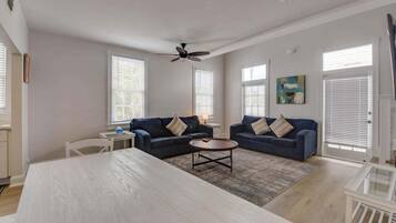 A spacious living room with two dark blue sofas, a round coffee table, and a white dining table.