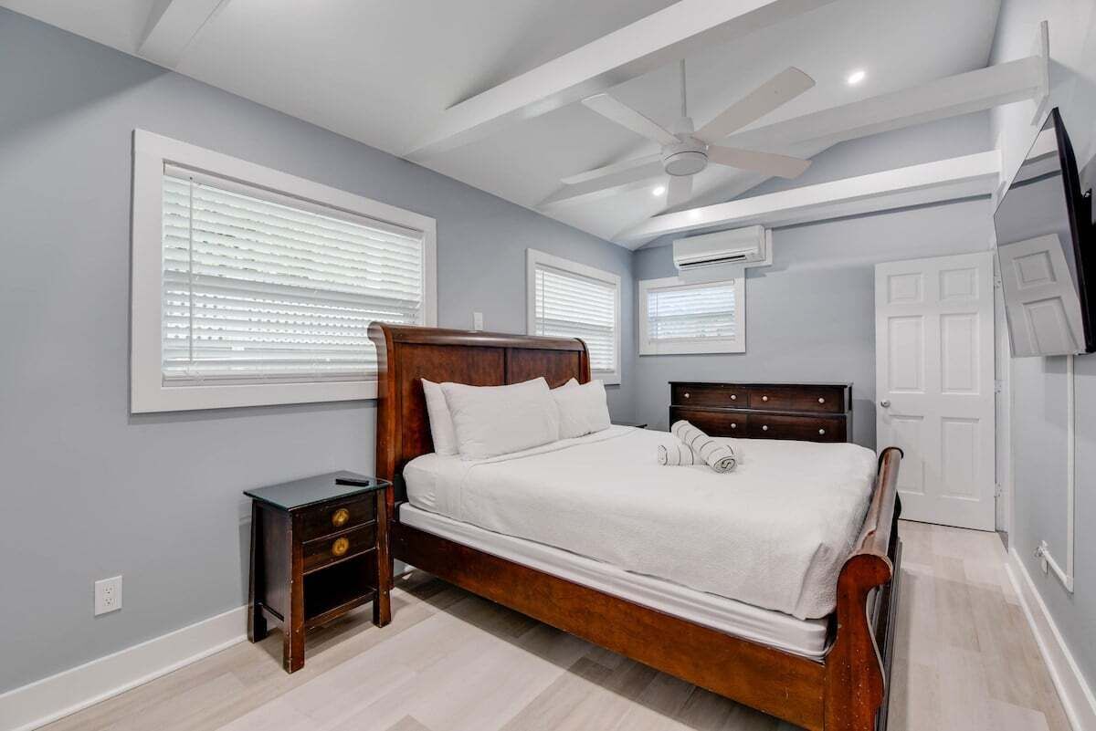 Camera da letto con un letto in legno, un comodino, una ventola a soffitto e una finestra con persiane.