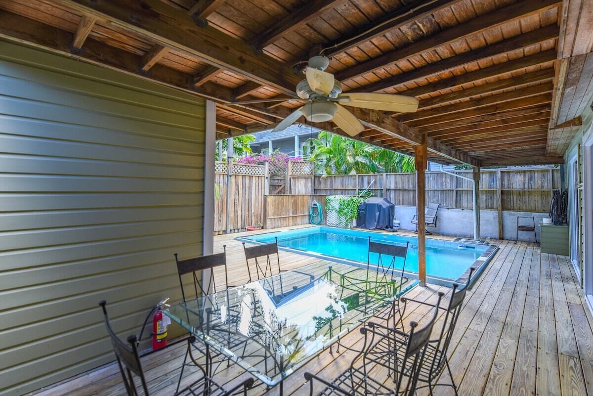 A covered outdoor area with a pool, wooden deck, and glass table with chairs.