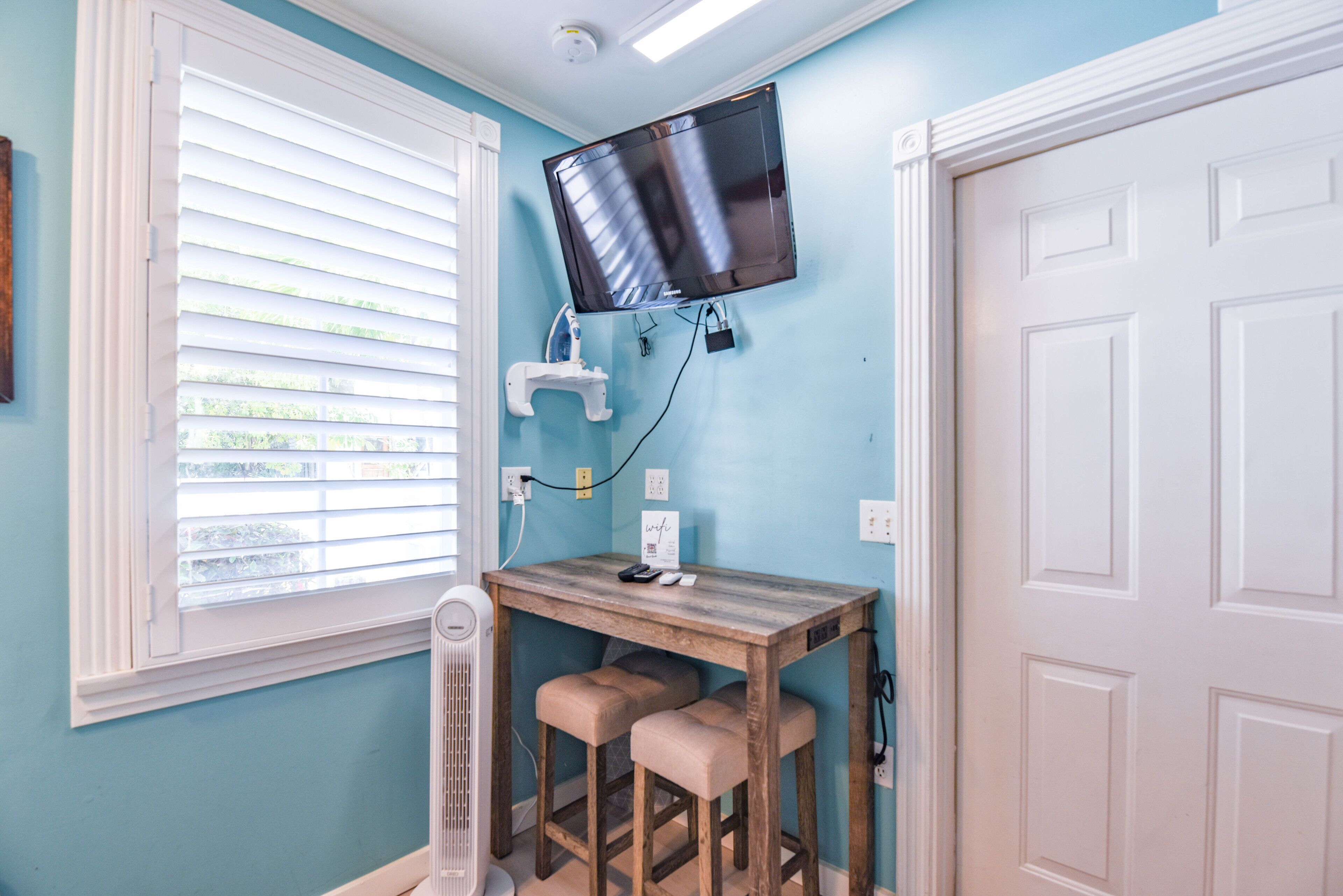 A room with a wooden table, two chairs, a mounted TV, and a white door.