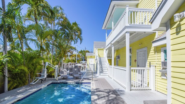 A pool area with a wooden deck, lounge chairs, and a staircase leading to a balcony. - Leo's Lodge | Newly Updated! (Key West)