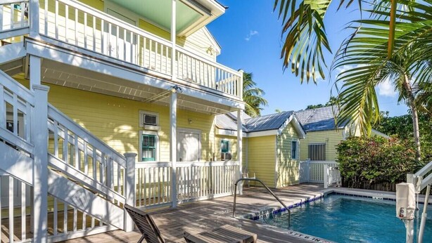 A two-story yellow building with a pool, wooden deck, and white railings. - Carey's Corner | Updated Studio with Heated Pool (Key West)
