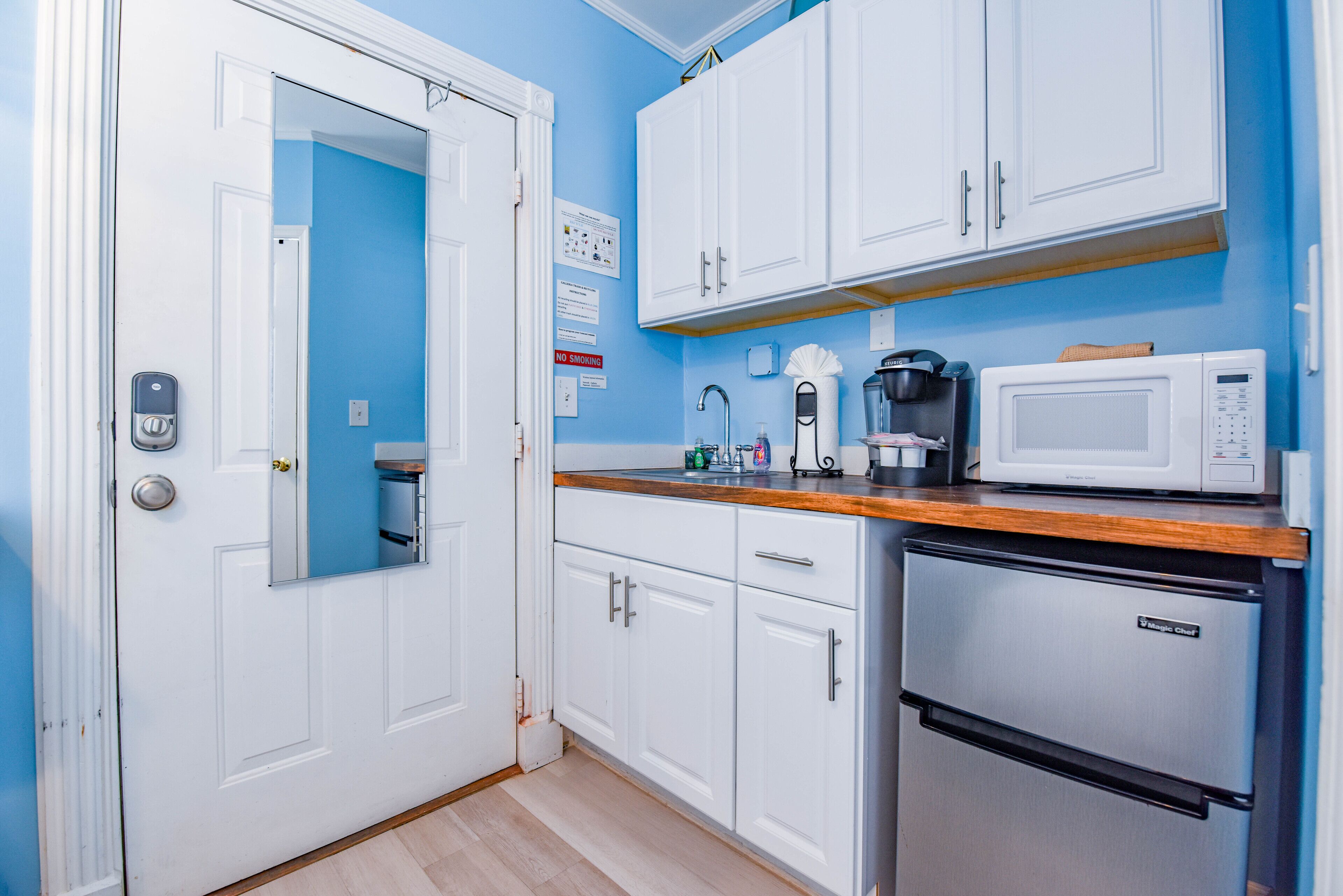 Una cocina compacta con armarios blancos, microondas, cafetera y refrigerador.