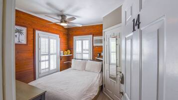 A bedroom with a bed, white walls, wooden paneling, a ceiling fan, and a door with the number 14.