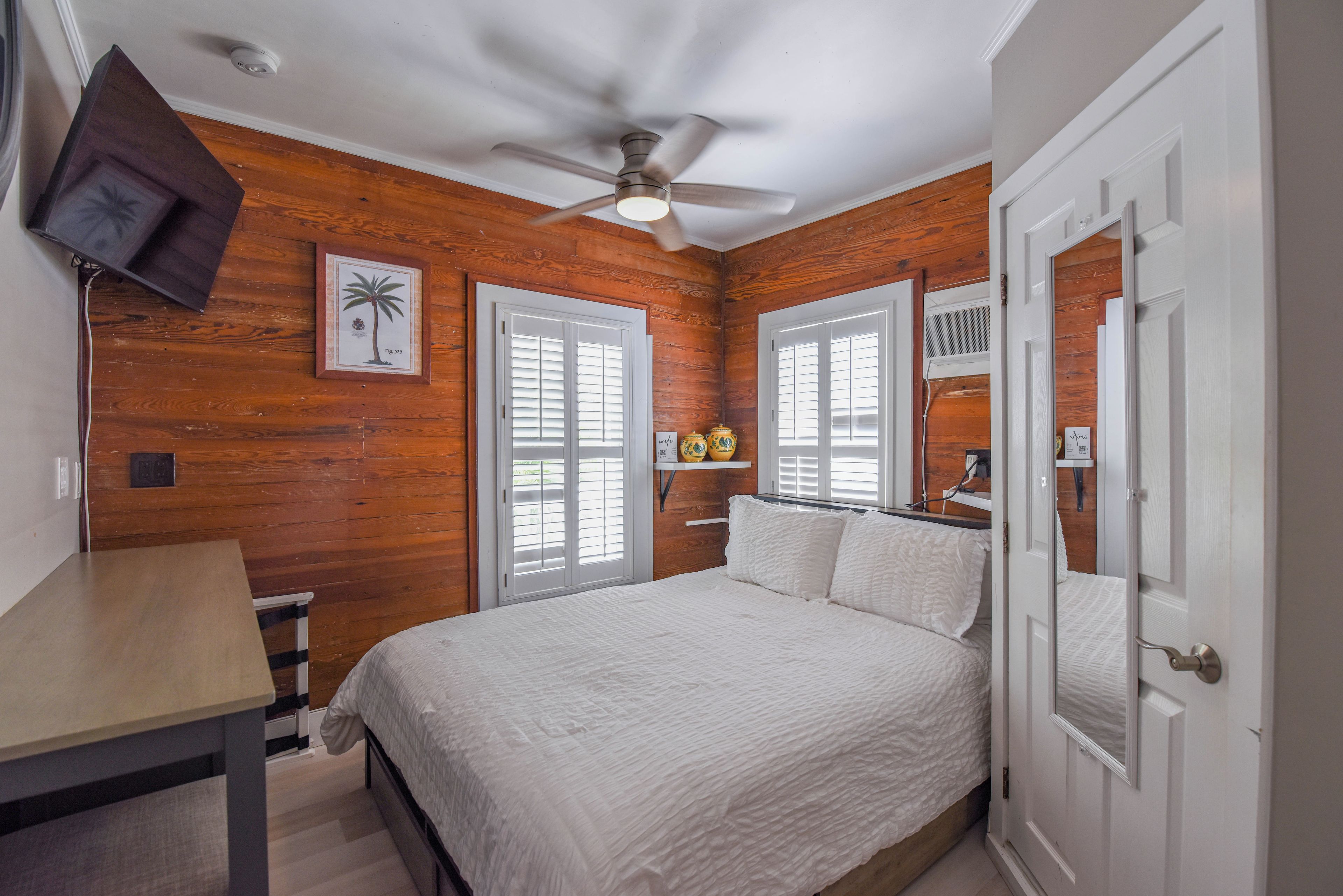 Un dormitorio con una cama, ventilador de techo, paredes de madera y una puerta.