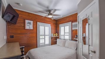 Un dormitorio con una cama, ventilador de techo, paredes de madera y una puerta.