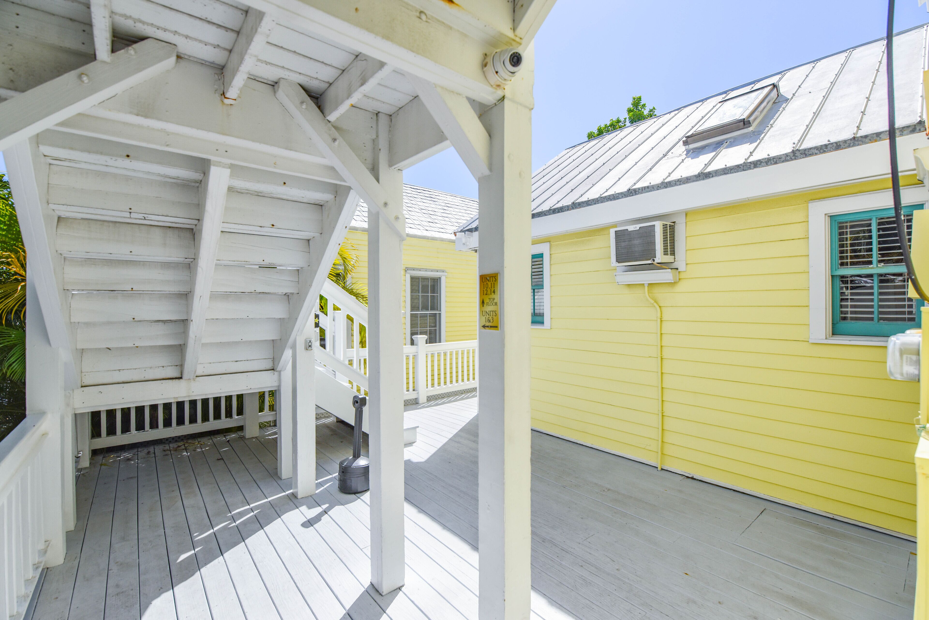 A covered wooden deck with a white railing, a yellow building with a metal roof, and a white fence.