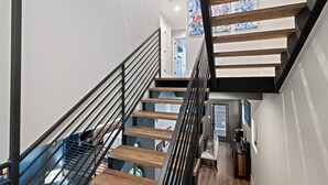 En moderne trappe med trætrin og sorte gelændere, der fører til en platform med et skrivebord og en stol.