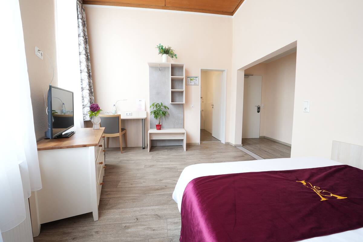 Une chambre d’hôtel avec un lit, un bureau, une chaise et une petite plante.