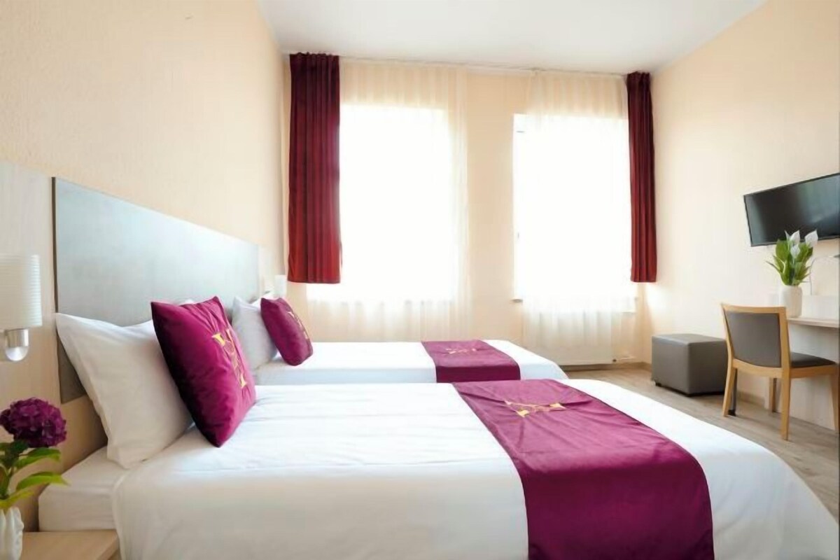 A hotel room with two beds, a TV, a desk, and a chair.