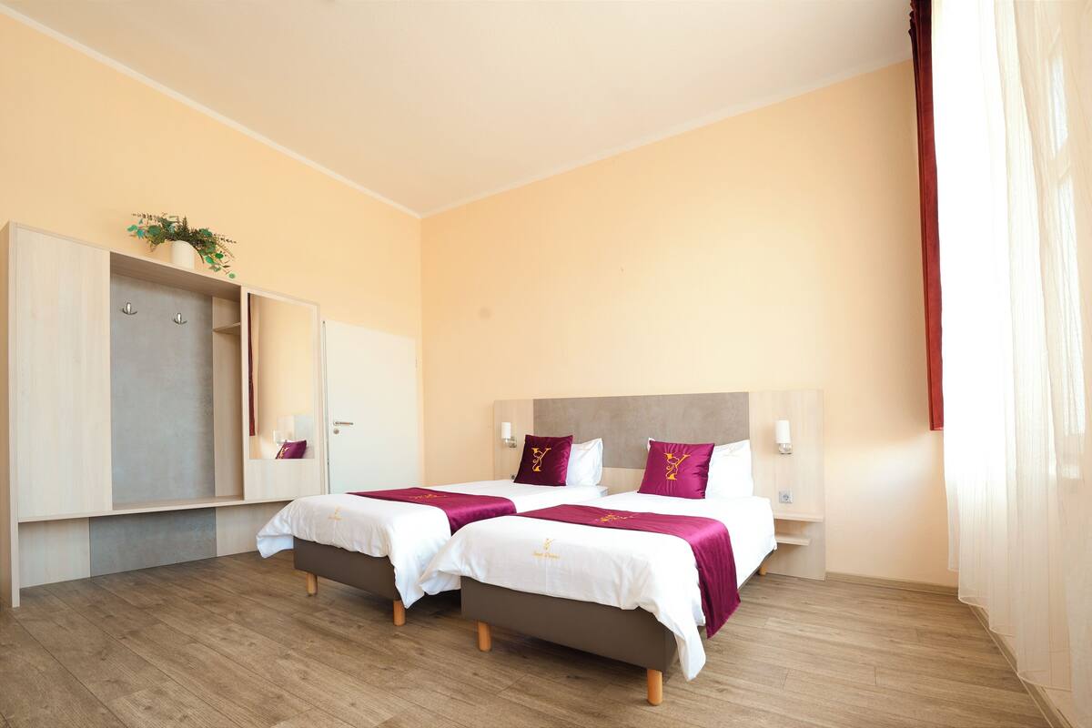Une chambre d’hôtel avec deux lits, une armoire, une table de chevet et une fenêtre avec des rideaux.