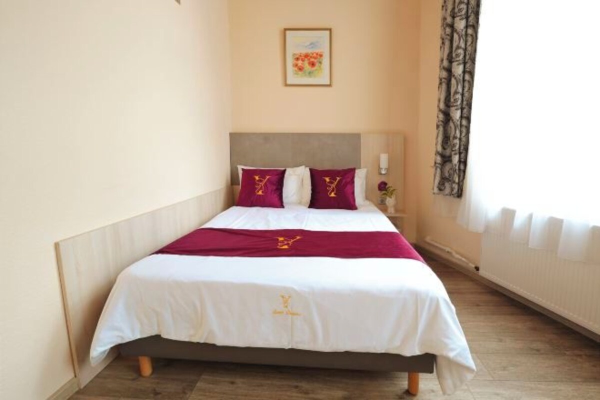 A neatly made bed with a white and maroon bedspread, a wooden headboard, and a framed picture on the wall.